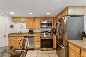 Kitchen with appliances with stainless steel finishes, light stone counters, a sink, recessed lighting, and light tile patterned flooring