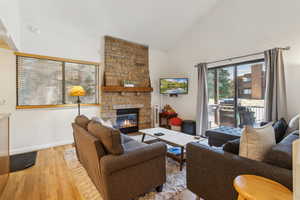 Living room with high vaulted ceiling, wood finished floors, a stone fireplace, and baseboards