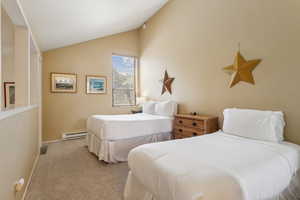 Carpeted bedroom featuring a baseboard heating unit, vaulted ceiling, and baseboards