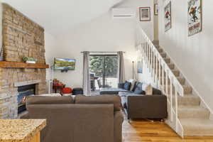 Living area with high vaulted ceiling, an AC wall unit, a fireplace, light wood-style flooring, and stairway