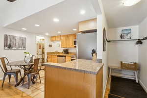 Kitchen featuring appliances with stainless steel finishes, light brown cabinetry, a sink, recessed lighting, and a peninsula
