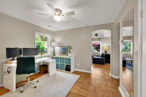 Office space featuring a ceiling fan, arched walkways, plenty of natural light, and baseboards