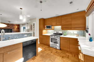 Kitchen with stainless steel appliances, backsplash, brown cabinetry, and light countertops