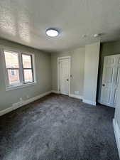 Spare room featuring a textured ceiling, a smoke detector, dark colored carpet, and baseboards