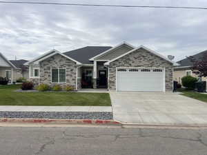 View of front facade featuring stone siding, a front lawn, driveway, and an attached garage