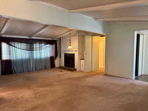 Unfurnished living room featuring beamed ceiling, carpet floors, and a fireplace with raised hearth