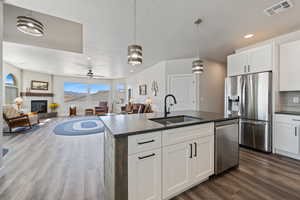 Kitchen with a sink, stainless steel appliances, dark wood finished floors, a glass covered fireplace, and a center island with sink