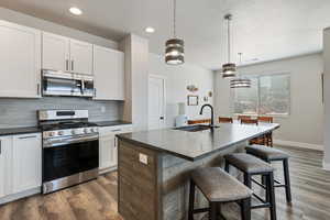Kitchen with appliances with stainless steel finishes, a sink, backsplash, baseboards, and a kitchen bar