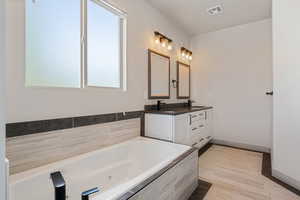 Bathroom featuring double vanity, a tub with jets, and baseboards
