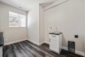 Laundry room with hookup for a washing machine, dark wood-style flooring, bar with sink, electric dryer hookup, and cabinet space