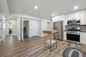 Kitchen with appliances with stainless steel finishes, dark countertops, baseboards, light wood-type flooring, and recessed lighting