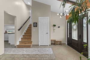 Foyer featuring high vaulted ceiling, stairway, a chandelier, and baseboards