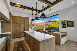 Kitchen with brown cabinets, stainless steel range, hanging light fixtures, beam ceiling, and light stone counters