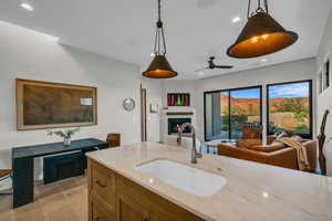 Kitchen featuring recessed lighting, open floor plan, light stone counters, a warm lit fireplace, and brown cabinetry