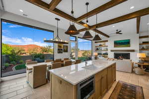 Kitchen featuring light stone counters, decorative light fixtures, beamed ceiling, open floor plan, and a lit fireplace