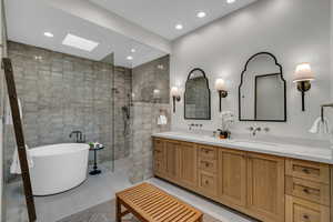 Full bathroom featuring a skylight, a freestanding tub, double vanity, light tile patterned floors, and walk in shower