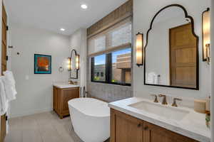 Bathroom featuring two vanities, a soaking tub, light tile patterned flooring, tile walls, and recessed lighting