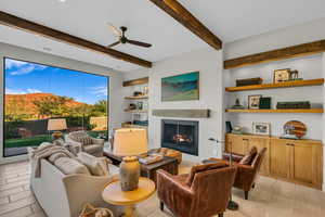Living area featuring a warm lit fireplace, ceiling fan, a mountain view, built in shelves, and beamed ceiling