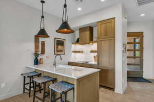 Kitchen featuring a kitchen breakfast bar, hanging light fixtures, backsplash, light stone countertops, and open shelves