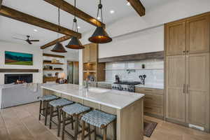 Kitchen with beam ceiling, a kitchen bar, decorative light fixtures, light stone counters, and a warm lit fireplace