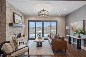 Living area featuring dark wood finished floors, a chandelier, a stone fireplace, recessed lighting, and baseboards