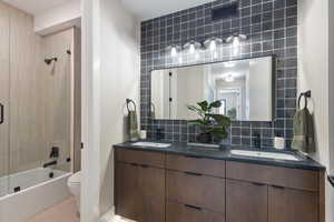 Bathroom with toilet, double vanity, shower / washtub combination, backsplash, and tile patterned floors