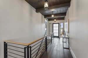 Corridor featuring an upstairs landing, wooden ceiling with exposed beams, dark wood-type flooring, and baseboards