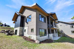 Back of property with stone siding, a balcony, and a yard