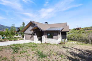 View of front of house with a standing seam roof, stone siding, driveway, metal roof, and a garage