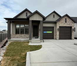 View of front of house with stone siding, board and batten siding, a front yard, concrete driveway, and an attached garage