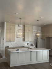 Kitchen with a chandelier, hanging light fixtures, light stone counters, and a kitchen island with sink