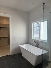 Full bath featuring tile walls, a soaking tub, wainscoting, dark tile patterned flooring, and a walk in closet