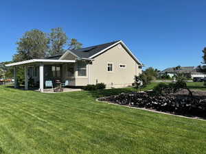 Back of house with a patio, roof mounted solar panels, a yard, and stucco siding