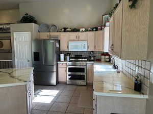 Kitchen with appliances with stainless steel finishes, a sink, backsplash, light brown cabinetry, and light tile patterned floors
