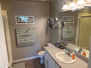 Bathroom with vanity, a stall shower, toilet, tile patterned floors, and baseboards