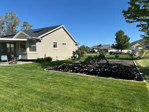 View of property exterior featuring a lawn, solar panels, stucco siding, and an outdoor fire pit
