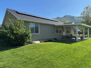 Back of house featuring roof mounted solar panels, stucco siding, a patio, a mountain view, and a yard