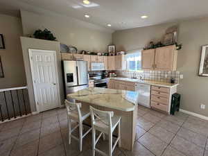 Kitchen with appliances with stainless steel finishes, light brown cabinets, tasteful backsplash, lofted ceiling, and light tile patterned floors