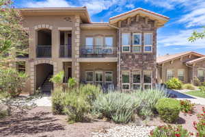View of front of home with stone siding, a balcony, stucco siding, a tile roof, and stairway