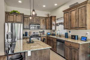 Kitchen featuring stainless steel appliances, a sink, a kitchen bar, light stone counters, and recessed lighting