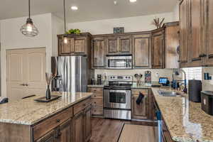 Kitchen with appliances with stainless steel finishes, a sink, light stone counters, dark wood finished floors, and a center island