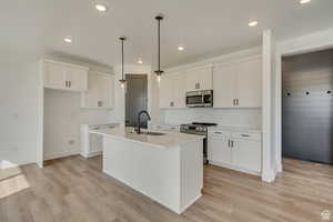 Kitchen with stainless steel appliances, a sink, light wood finished floors, a center island with sink, and recessed lighting