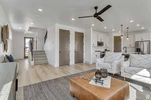 Living room with a ceiling fan, light wood-style flooring, baseboards, recessed lighting, and stairway