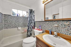 Bathroom with tile walls, shower / tub combo with curtain, vanity, and toilet