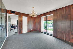 Unfurnished room with a chandelier, wooden walls, carpet flooring, and a textured ceiling