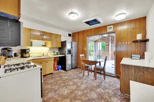 Kitchen featuring stainless steel fridge with ice dispenser, gas range oven, a sink, wood walls, and light countertops