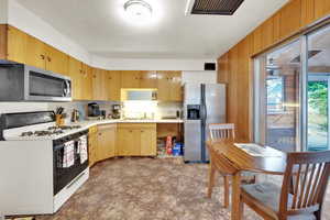 Kitchen featuring appliances with stainless steel finishes, tasteful backsplash, light countertops, wood walls, and a sink