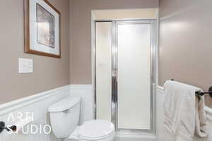 Bathroom with wainscoting, a stall shower, and toilet
