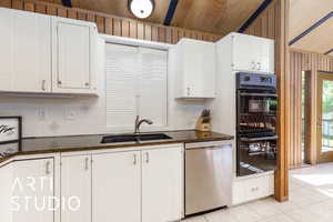 Kitchen featuring dishwasher, a sink, backsplash, light tile patterned floors, and dark stone counters