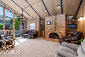 Carpeted living room with wooden walls, lofted ceiling, ceiling fan, and a brick fireplace
